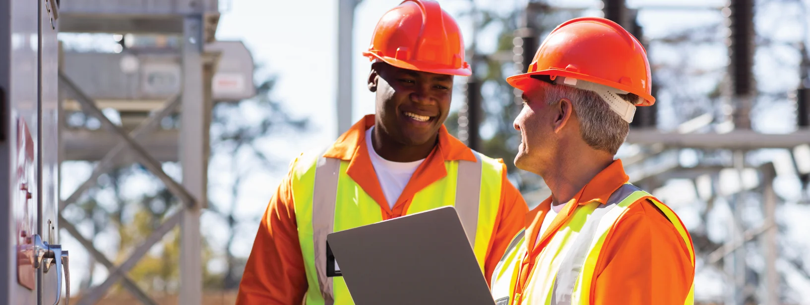 Two male utility construction workers wearing bright orange and hard hats